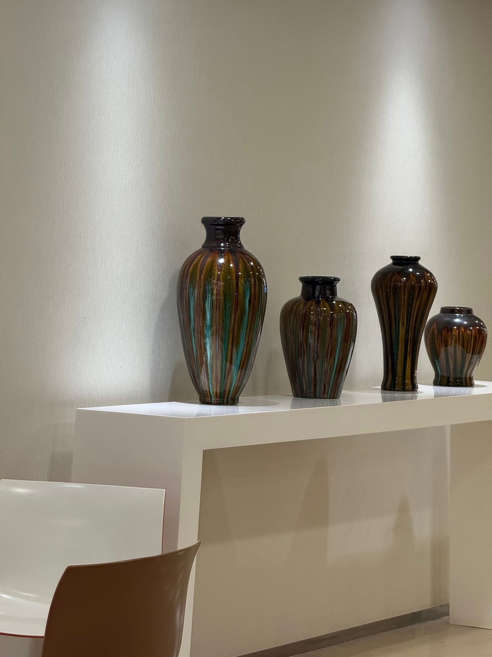 Four dark glazed ceramic vases in different sizes on a white console shelf