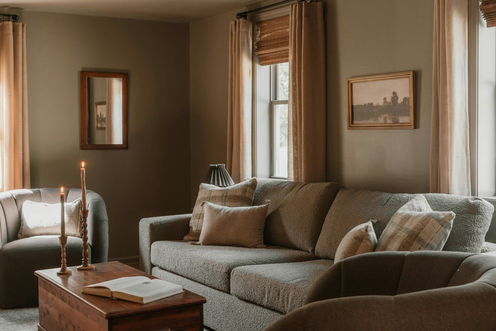 A cozy neutral living room with a sofa, armchair, pillows and candles