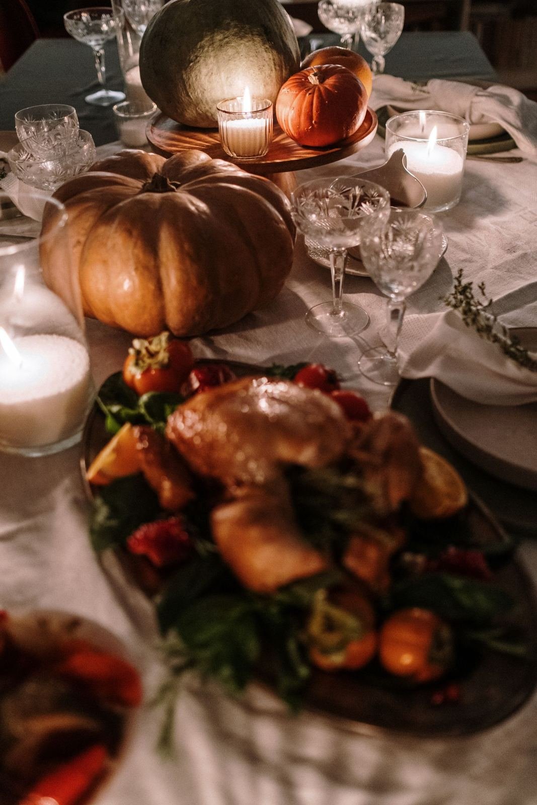 A candlelit Thanksgiving table with pumpkins, linen and crystal glasses